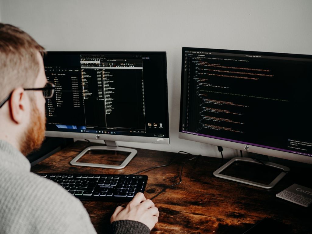 An engineer working at a desk in front of several monitors of code