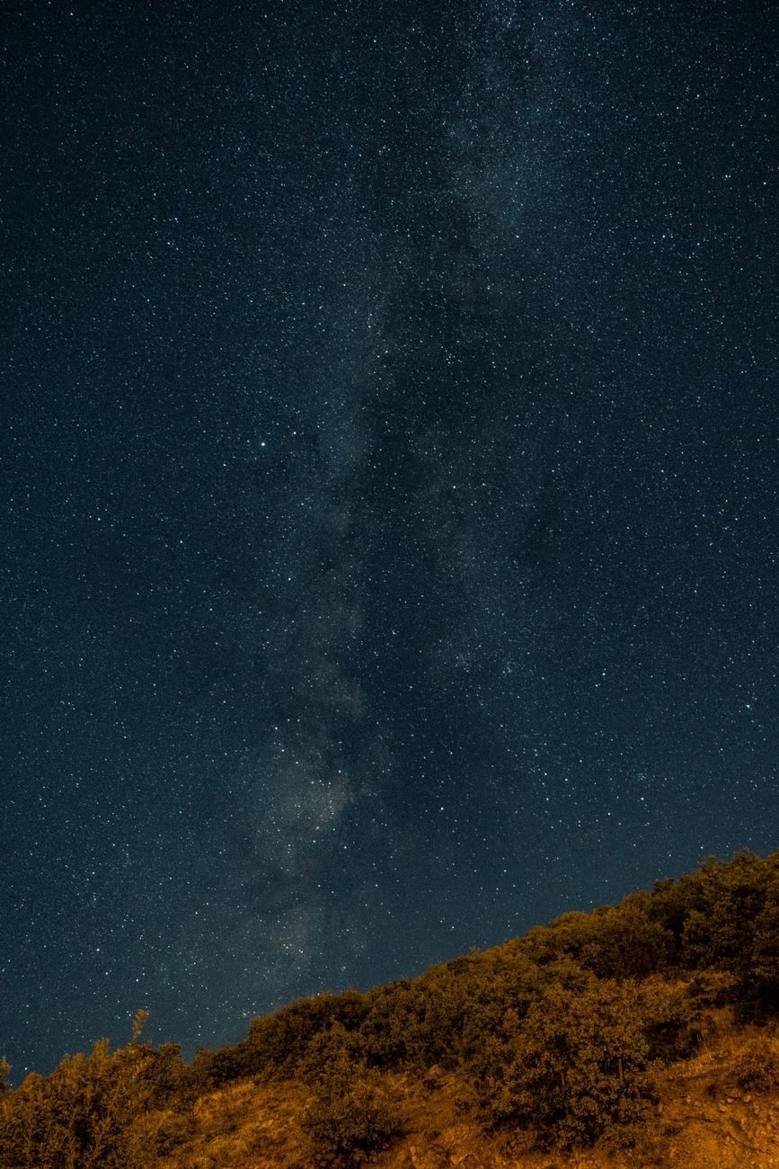 The Milky Way spread across a deep blue night sky above dark desert hills